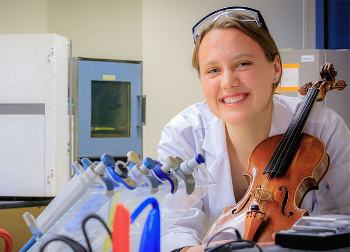 Student Kate Roberge with violin and lab equipment